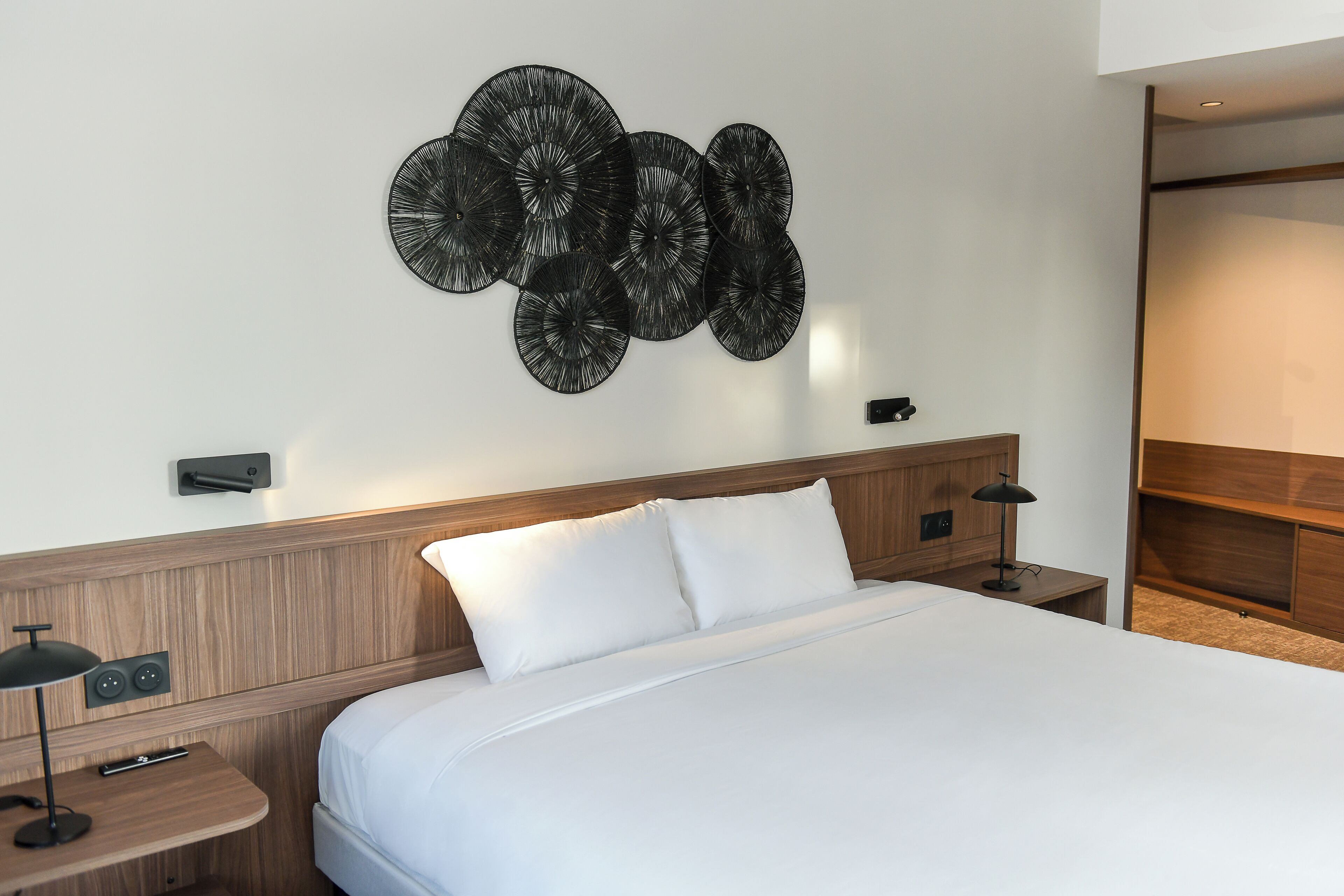 A neatly made bed with white linens, a wooden headboard, and a wall-mounted decorative piece.