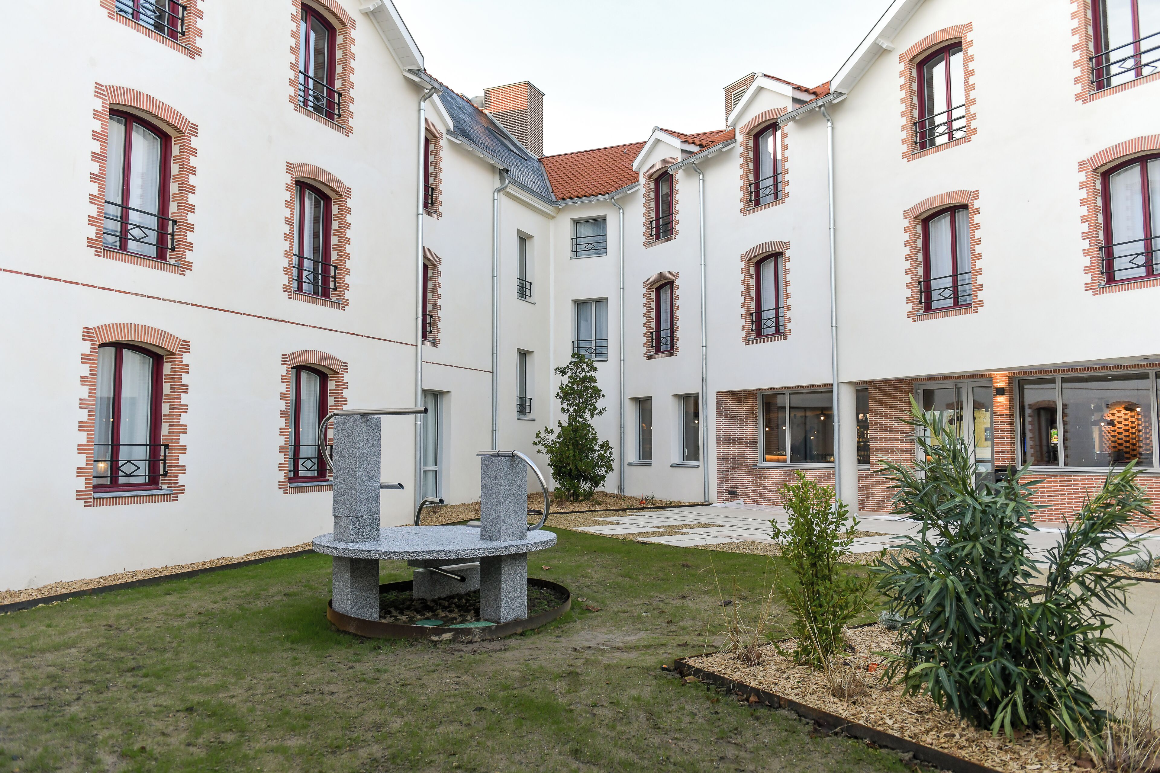A courtyard with a stone fountain, surrounded by buildings with brick accents and multiple windows.