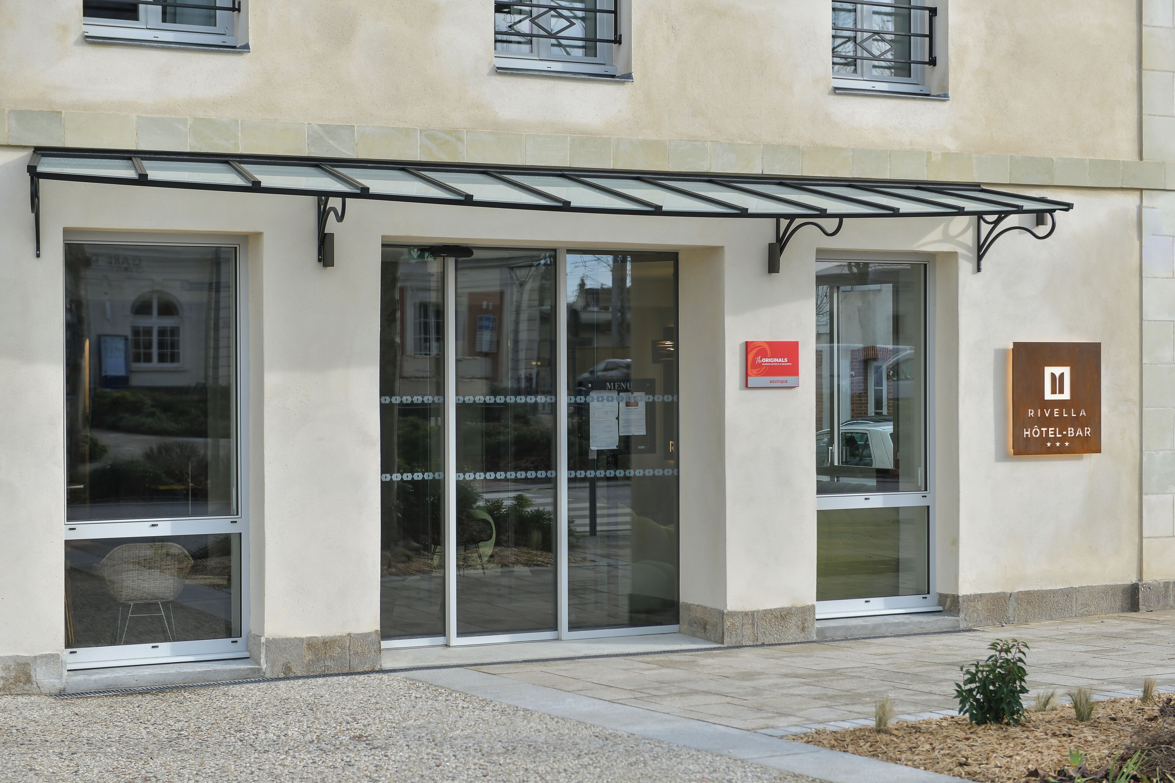 A hotel entrance with glass doors, a signboard, and a small garden area.