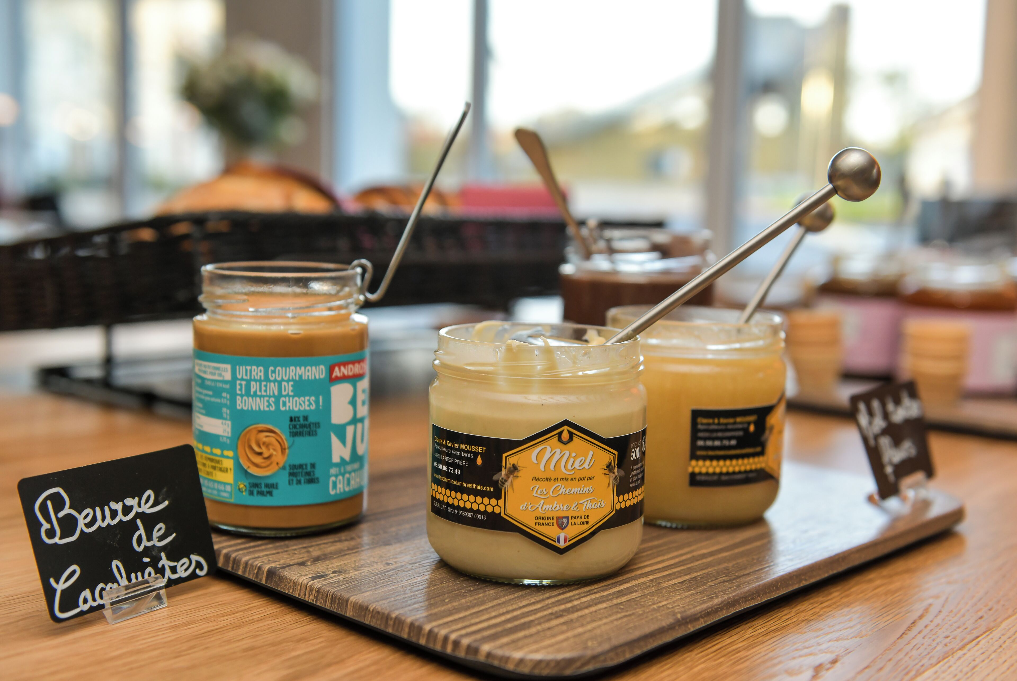 Three jars of honey on a wooden tray with labels and a sign indicating 'Beurre de Lacuètes'.