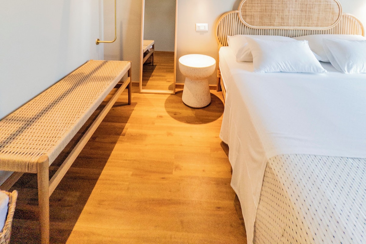 A modern bedroom with a wooden bench, a round toilet, and a bed with white bedding.