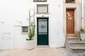 A white building with a green door, a potted plant, and a small window with a decorative grille. - Casetta Carlotta by Rentbeat (Ostuni)