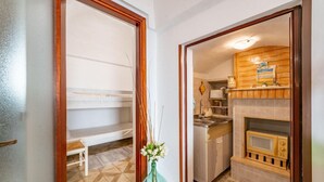 A room with a wooden bench, a vase with flowers, a kitchen with a microwave, and a tiled floor.