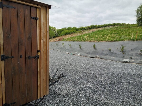 A wooden shed with metal hinges and a gravel driveway leading to a garden with young plants.