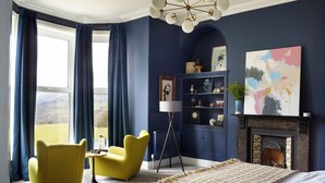Ein Schlafzimmer mit einem großen Bett, einem gelben Sessel, einem blauen Sessel, einem Bücherregal und einem Kamin.