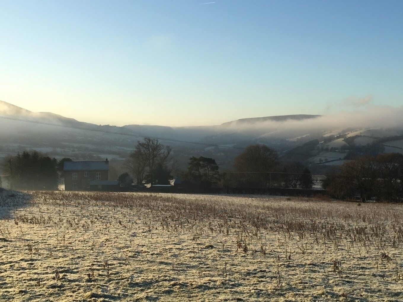 A rural landscape with a farmhouse, fields, and rolling hills in the background.