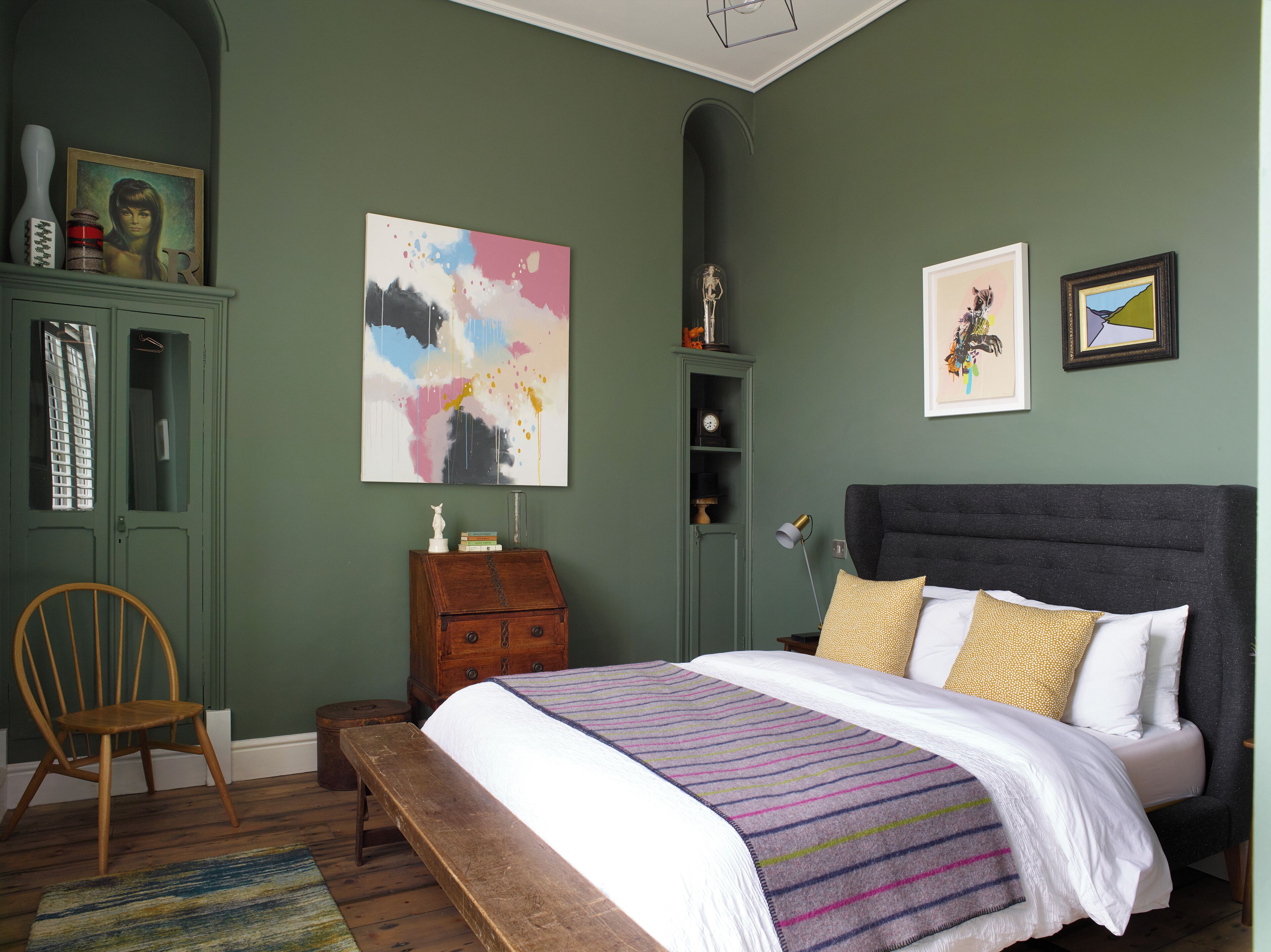 Un dormitorio con cama, una silla, cómoda y obras de arte en las paredes.