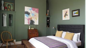 Un dormitorio con cama, una silla, cómoda y obras de arte en las paredes.