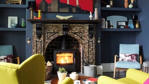 Ein Wohnzimmer mit Kamin, zwei gelbe Sessel, einem roten abstrakten Gemälde und Regalen mit Dekorationsobjekten.