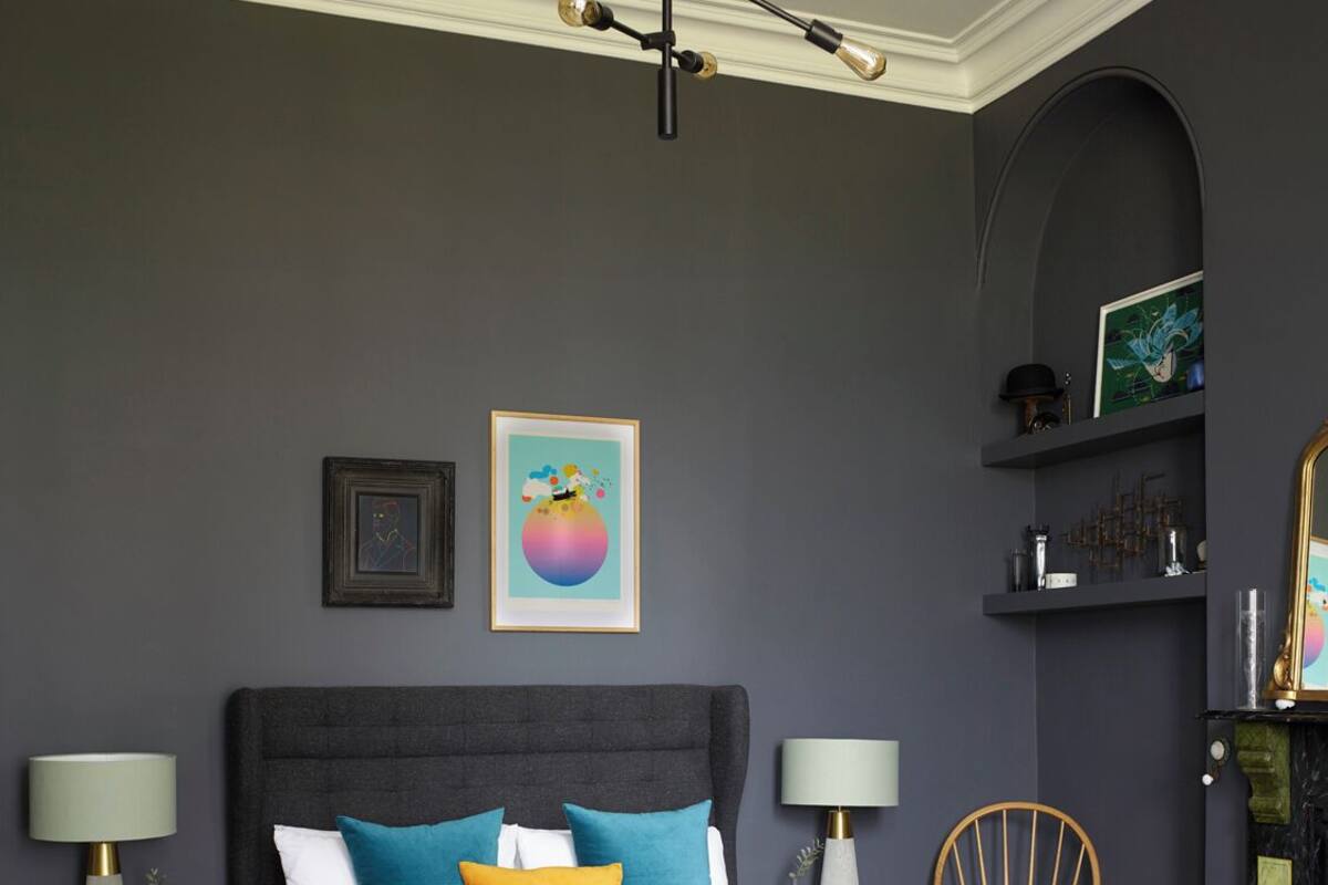 Un dormitorio con cama, dos mesitas de noche, una silla, estante en la pared y lámpara en el techo.