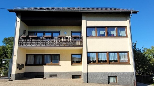 Een gebouw met twee verdiepingen, een balkon op de bovenverdieping, een ingang op de begane grond en een klein raam aan de rechterkant.