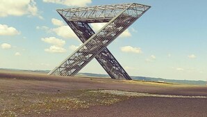 Een grote, metalen X-vormige constructie in een open veld.