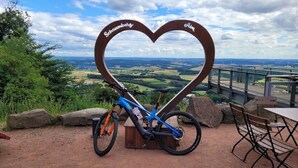 Een mountainbike geparkeerd voor een hartvormig bord met 'Saunberg' en 'Ain' erop, met uitzicht op een schilderachtig landschap.