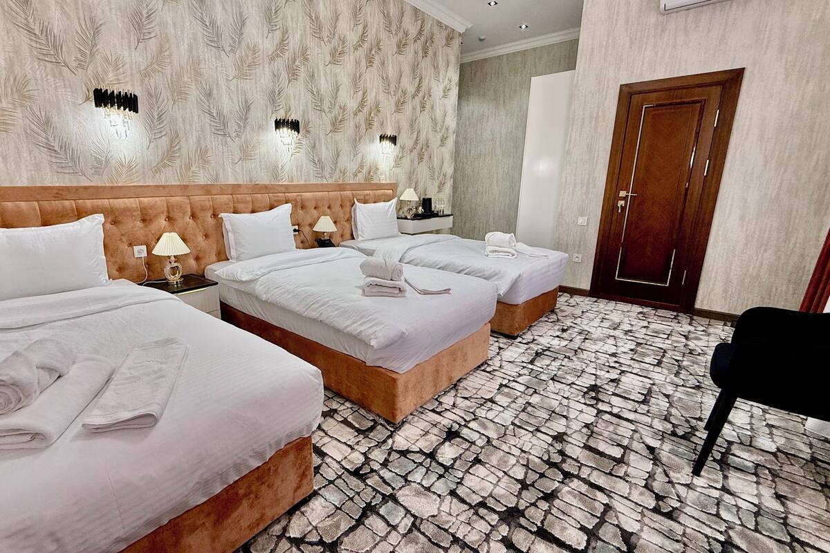 Habitación de hotel con dos camas, cabecero de madera, papel tapiz estampado, suelo con diseño de piedra y una puerta.