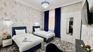 A hotel room with two beds, a chandelier, a mirror, and a patterned floor. - Maksima (Samarkand)