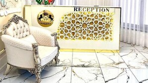 A reception area with a marble floor, a chandelier, a reception desk, and a decorative chair. - Maksima (Samarkand)