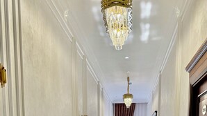 A hallway with a polished floor, decorative wall moldings, a chandelier, and a door with a number plate. - Maksima (Samarkand)