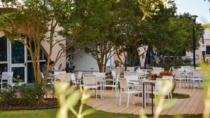 An outdoor seating area with white chairs and tables, surrounded by trees and a building with large windows. - Coastal family paradise - step right onto the sand (Bibione)