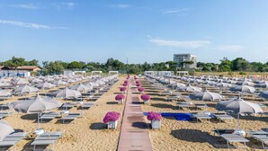 Une plage bordée de rangées de chaises longues et de parasols, une allée centrale et un bâtiment en arrière-plan.