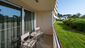 Un balcon avec une table et des chaises, donnant sur un jardin bien entretenu et sur un bâtiment situé au loin.