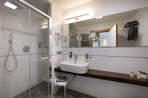Un baño moderno con ducha envuelta en vidrio, un lavabo blanco y un espejo grande.
