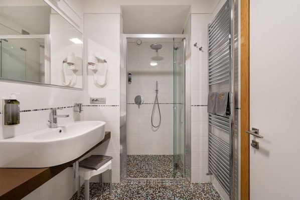 Un baño moderno con un lavamanos blanco, una cabina de ducha con mampara de vidrio y un perchero con toallas.