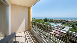 Un balcón con vistas despejadas a una piscina, playa y paisaje lejano.
