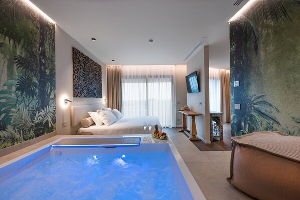 Una habitación de hotel con una cama grande, una zona de estar pequeña, un televisor y un mural grande en la pared.