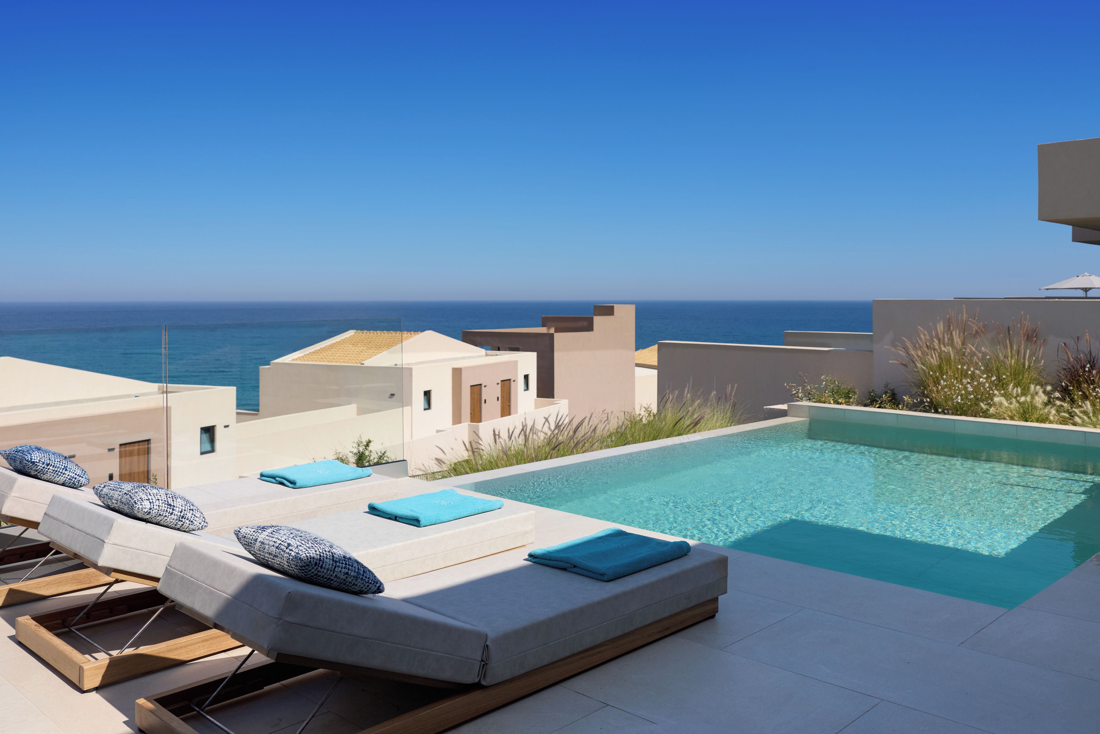 Área de piscina en la azotea con sillones y vista al mar.
