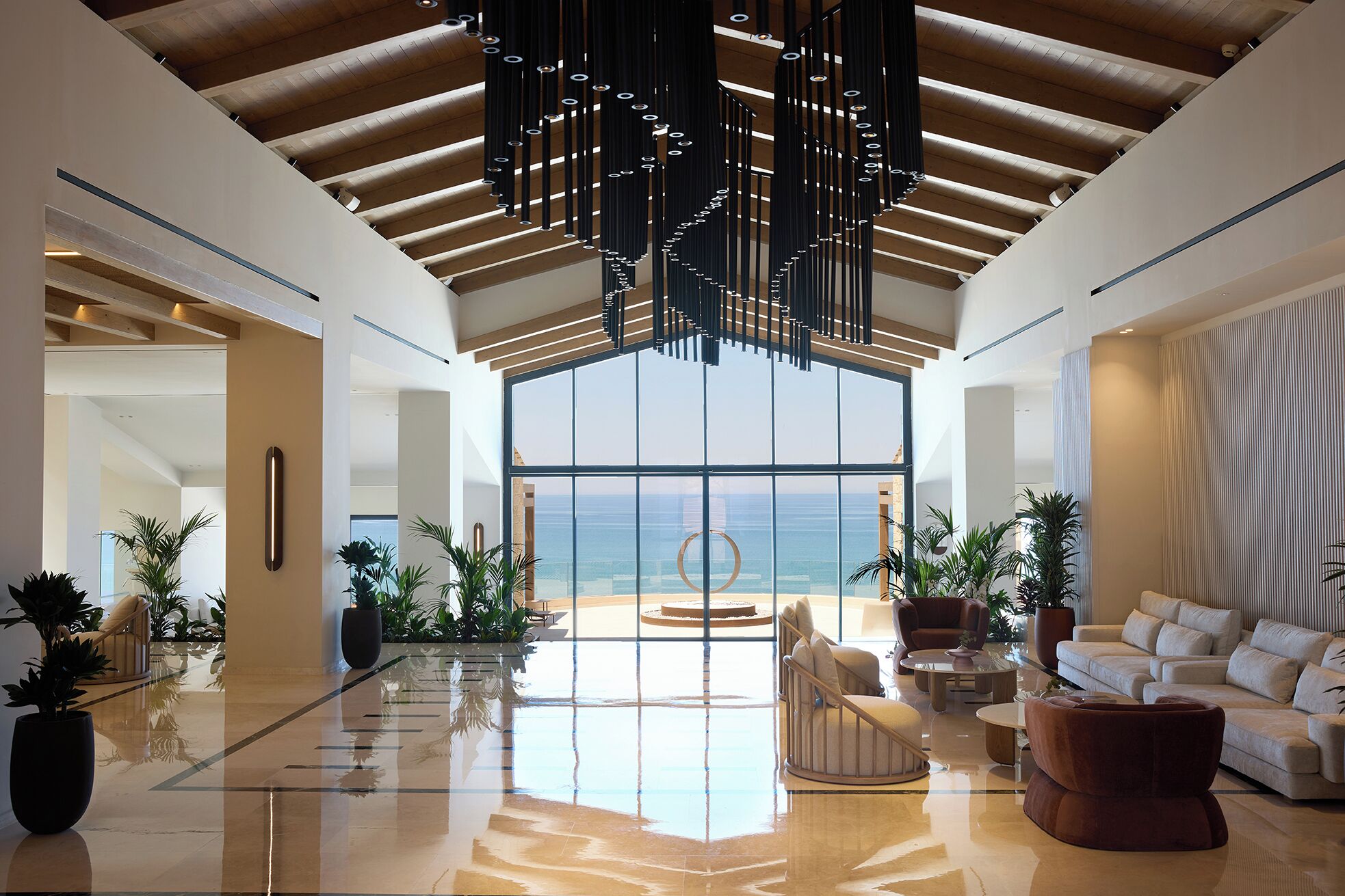 A spacious lobby with a high ceiling, large windows offering a view of the sea, and modern furnishings.