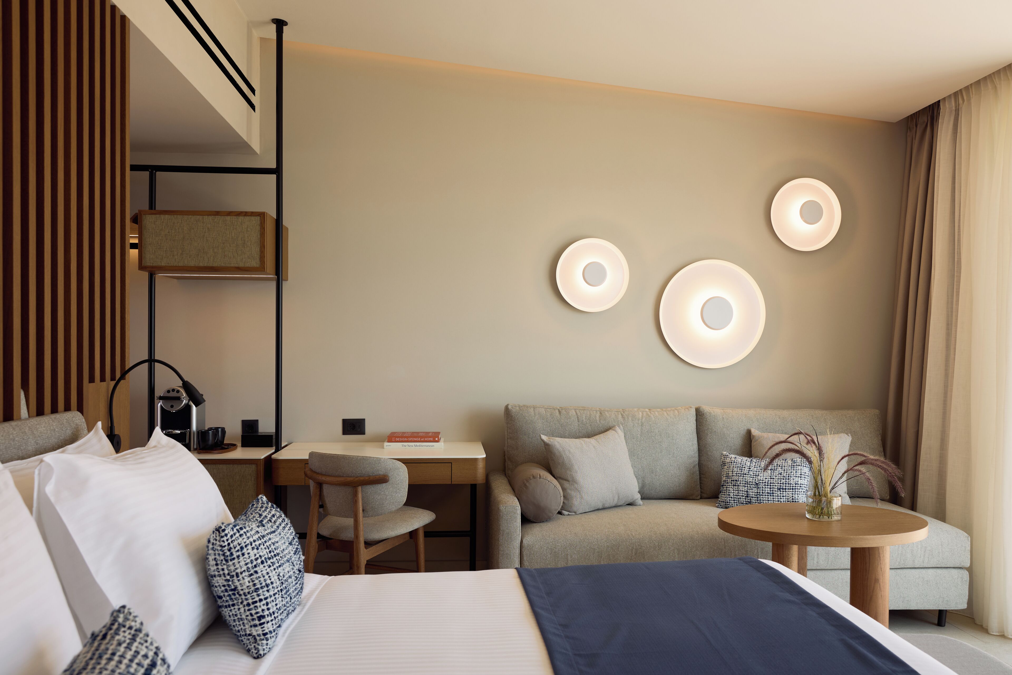 A modern hotel room with a bed, a sofa, a desk, and a small table.