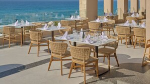 An outdoor dining area with tables and wicker chairs, overlooking the sea.