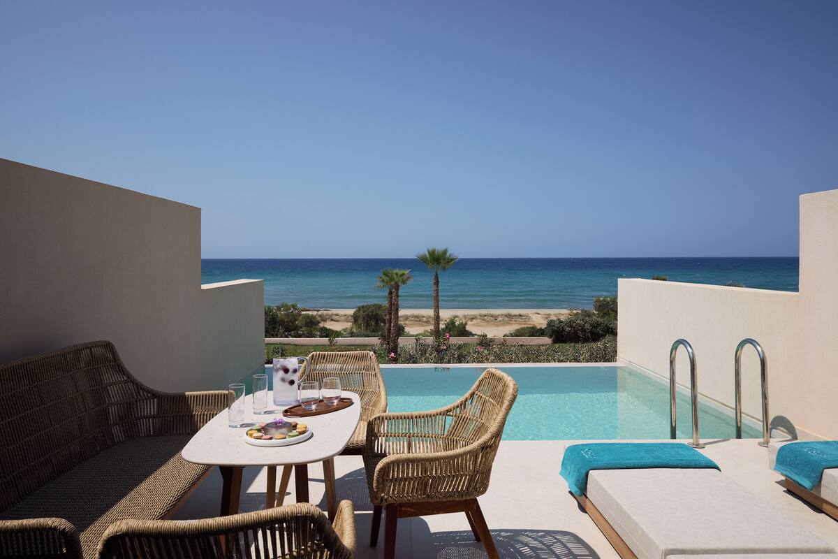 Ein Poolbereich mit Korbmöbeln, einem Tisch mit Gläsern und einem Teller sowie Blick auf das Meer.
