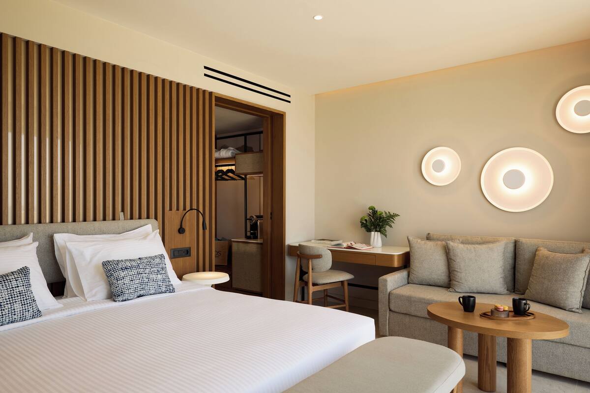 Ein modernes Hotelzimmer mit einem großen Bett, einer Wandpaneele aus Holz, einem Schreibtisch, einem Sofa und einem runden Couchtisch.