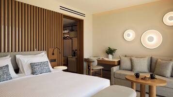 A modern hotel room with a large bed, a wooden panel wall, a desk, a sofa, and a round coffee table.