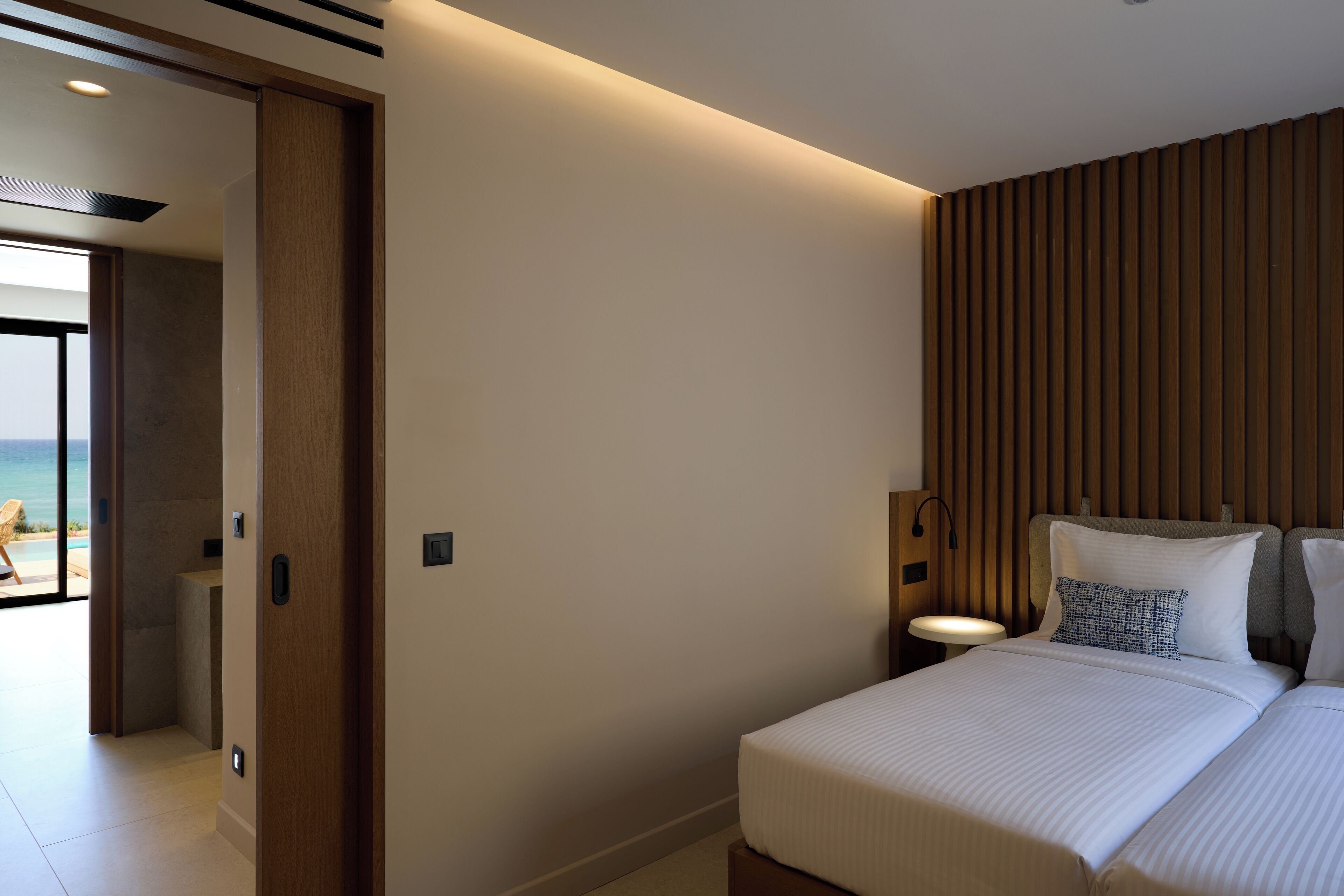 Una habitación de hotel moderna con una cama grande, un panel de pared de madera, una mesita de noche y vistas a la playa.