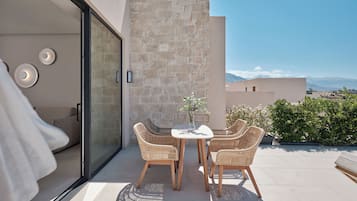 Un área de estar moderna al aire libre, con puerta de vidrio que da a un balcón, paredes de piedra y vistas a montañas lejanas.