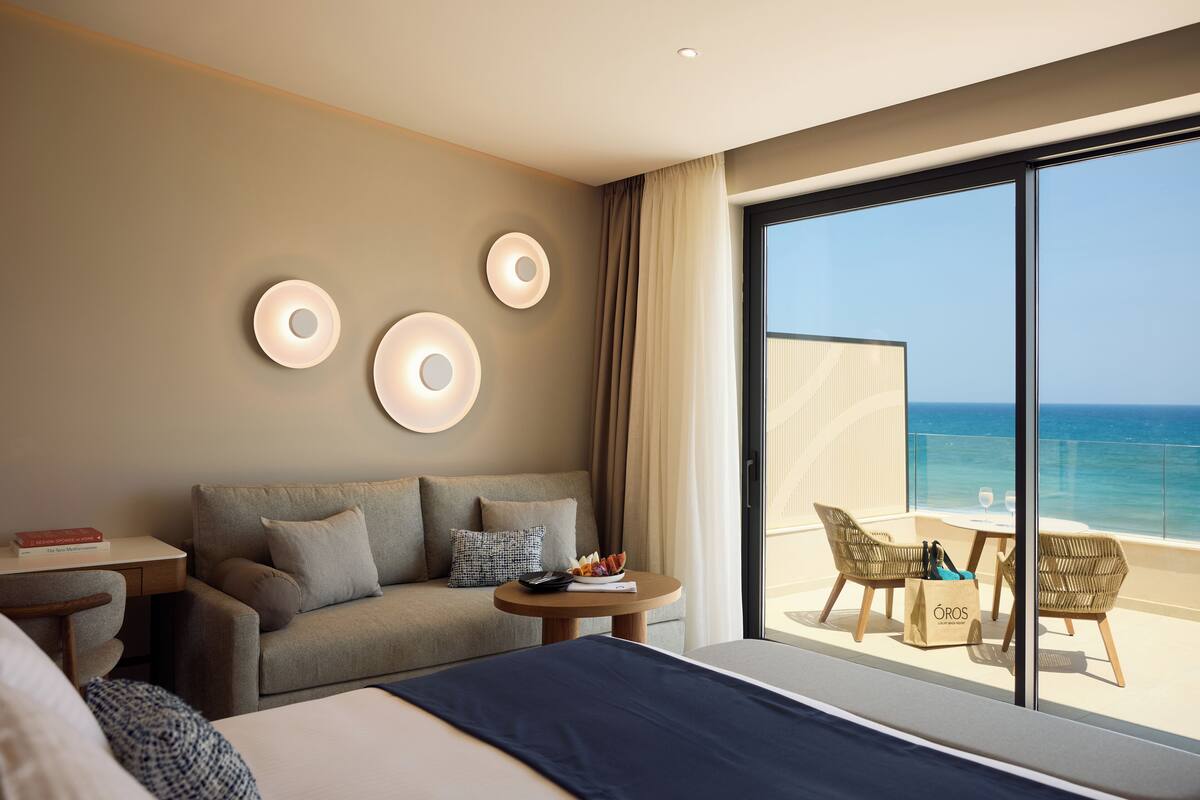 Ein Hotelzimmer mit Bett, Sofa, einem kleinen Tisch mit Obstschale und einem Balkon mit Korbstühlen und Tisch.