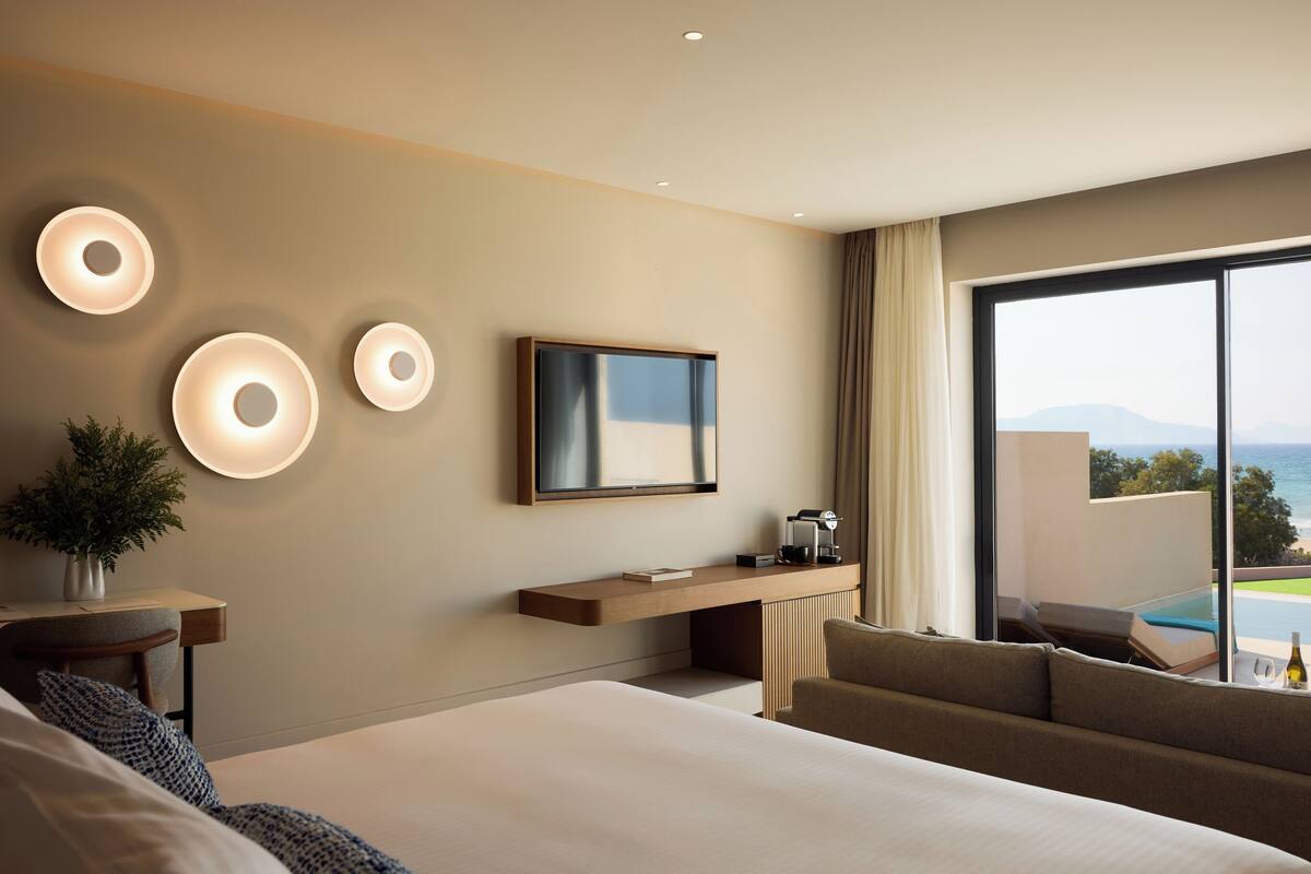 Ein modernes Hotelzimmer mit einem großen Bett, einer Couch, einem Fernseher und einem Balkon mit Blick auf einen Pool.