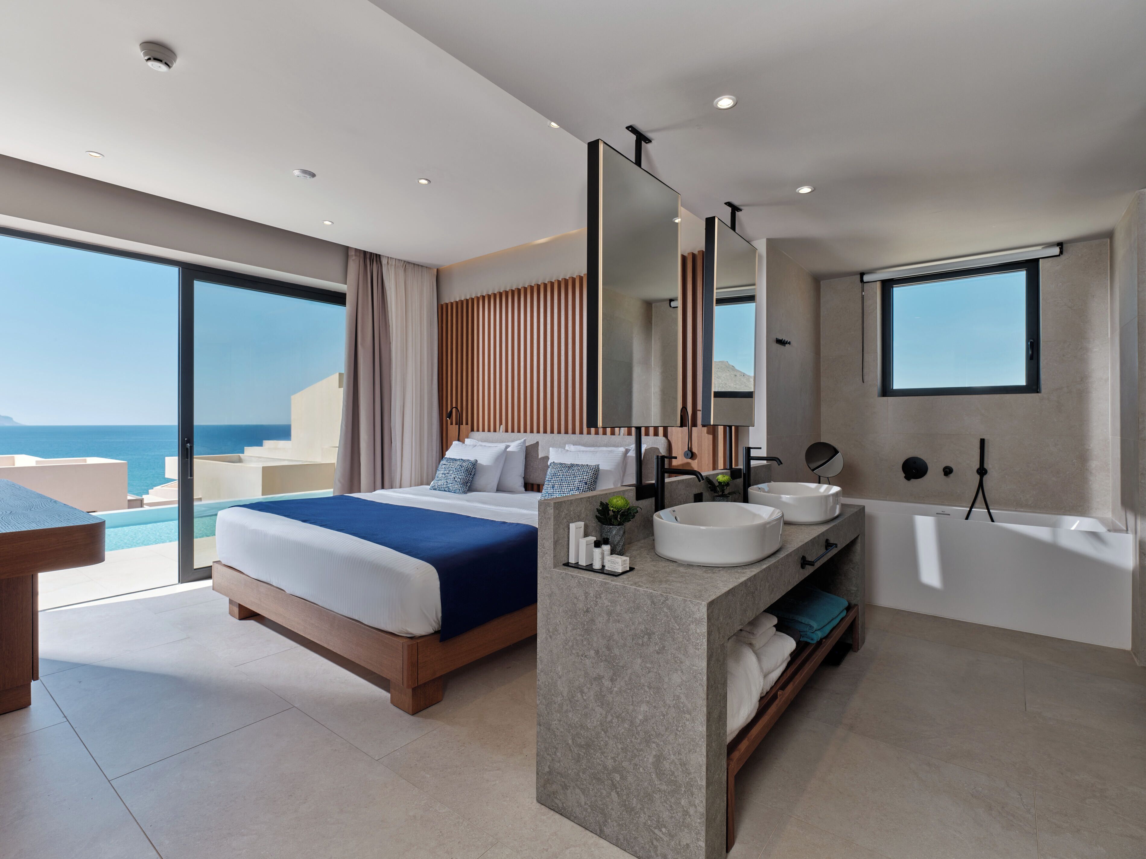 Een moderne hotelkamer met een groot bed, een badkamer met bad en uitzicht op zee.