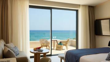 A hotel room with a bed, a sofa, a dining table with chairs, and a view of the ocean through a sliding glass door.