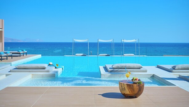 A poolside area with lounge chairs and a wooden bowl with fruit and a drink.