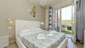 A bedroom with a large bed, a chandelier, a sliding glass door to a balcony, and decorative wall art. - My Peschiera Holiday Apartment- Quadrivium 3 (Castelnuovo del Garda)