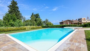 A rectangular swimming pool with a tiled deck, surrounded by a well-maintained lawn and trees. - My Peschiera Holiday Apartment- Quadrivium 3 (Castelnuovo del Garda)