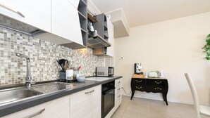 A modern kitchen with a tiled backsplash, stainless steel sink, and a built-in oven. There is a black and white cabinet with a microwave and toaster on the counter. - My Peschiera Holiday Apartment- Quadrivium 3 (Castelnuovo del Garda)