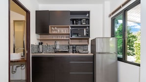Cucina moderna con mobili scuri, frigorifero in acciaio inossidabile e una finestra che offre vista sul verde.