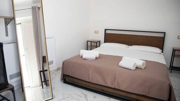 A neatly made bed with white and brown linens, a small bedside table, and a large mirror on the left.