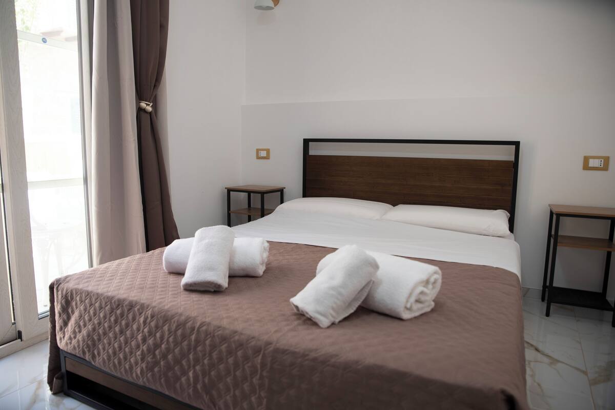 A neatly made bed with a brown quilt, two rolled towels, and a wooden headboard.