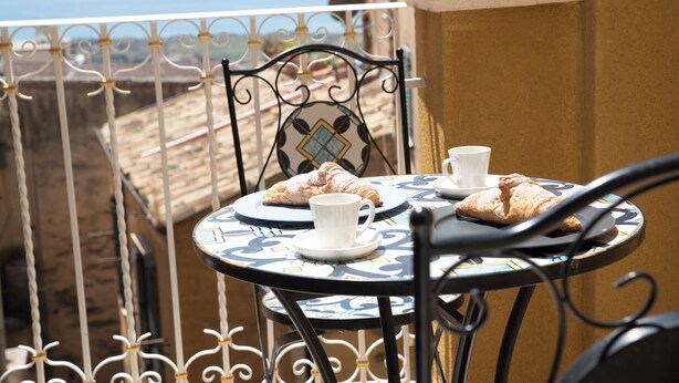 Una mesa con un croissant y una taza en un balcón con vista al mar.