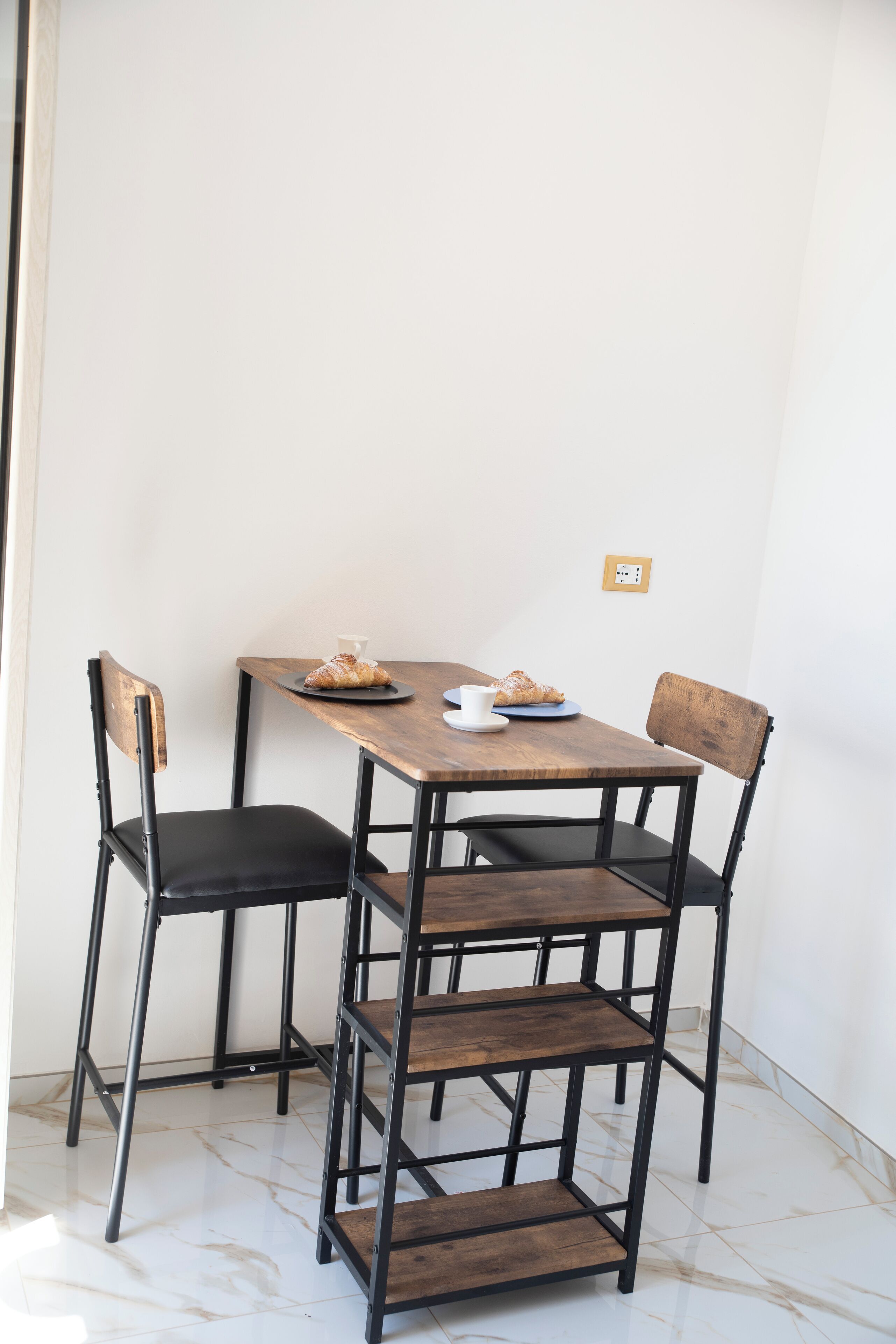 Un comedor con una mesa de madera, dos sillas y una estantería.